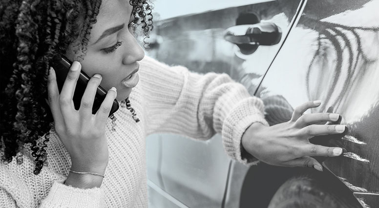 A woman looks at the damage on her car while talking on the phone