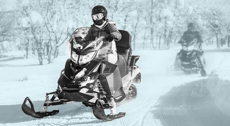 Two snowmobilers follow each other on a trail