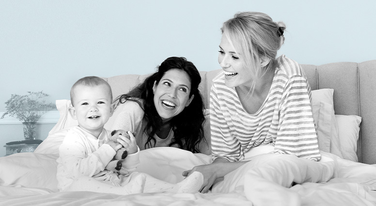 deux femmes souriantes et un bébé sur un lit