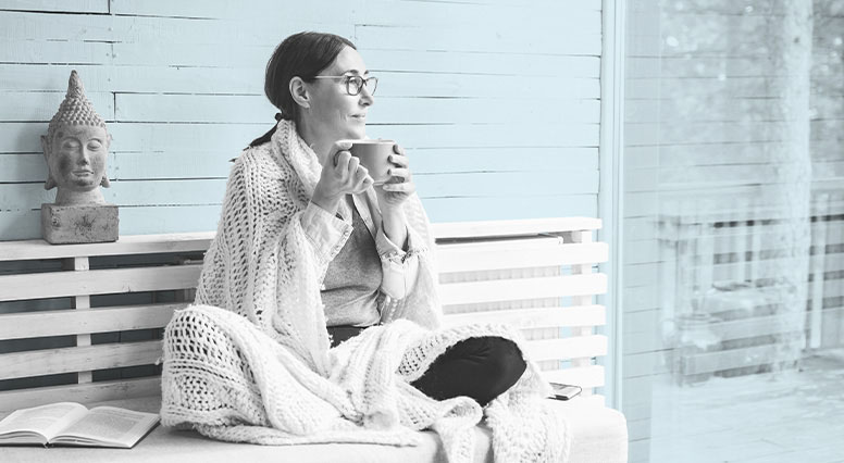 A woman sipping coffee under a blanket